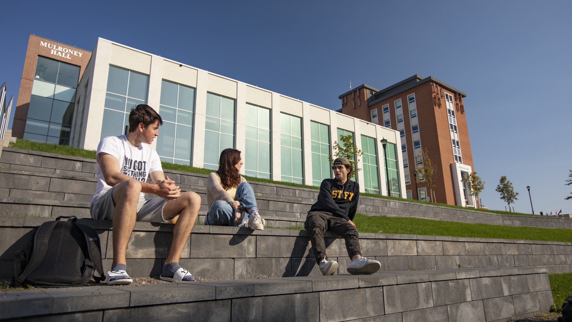 Students sitting on the brick located behind Mulroney Hall on a sunny day.