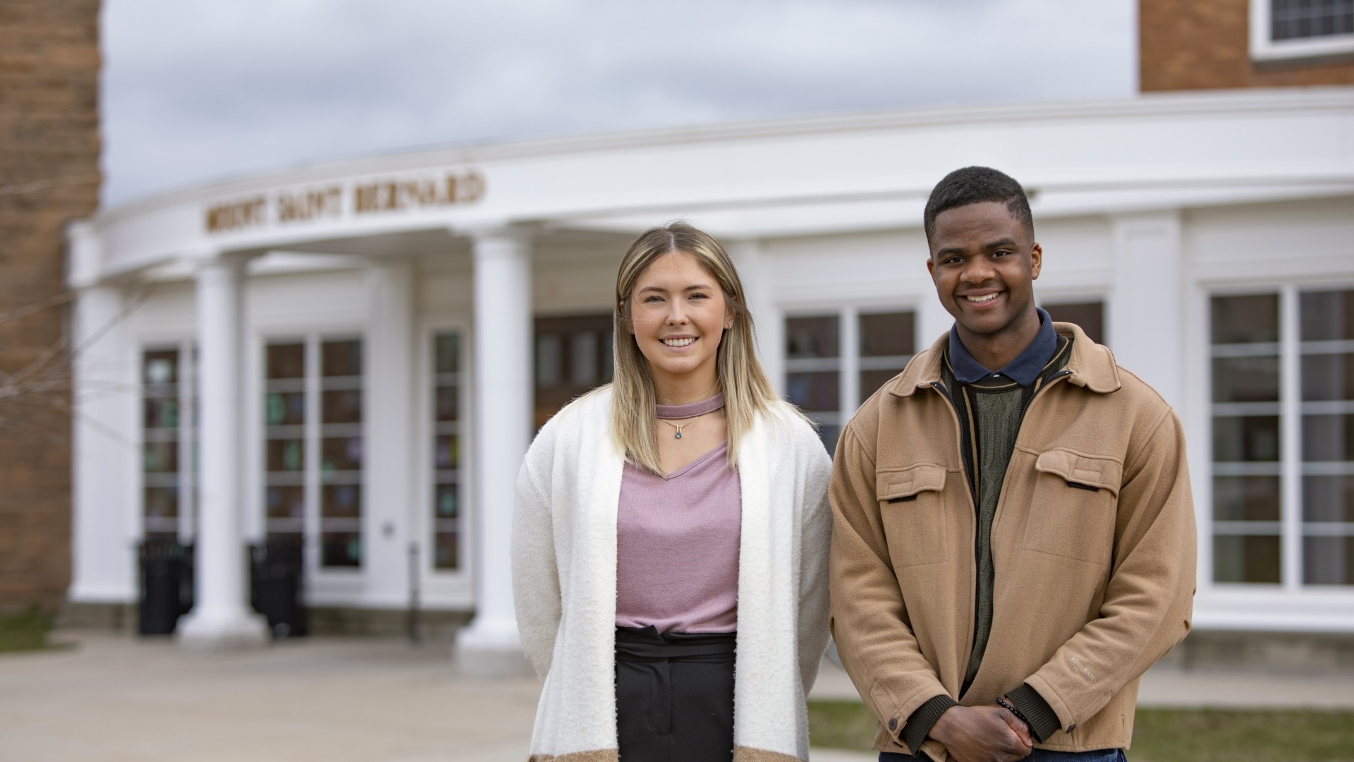 Two students photographed in front of Mount Saint Bernard on a cloudy day.