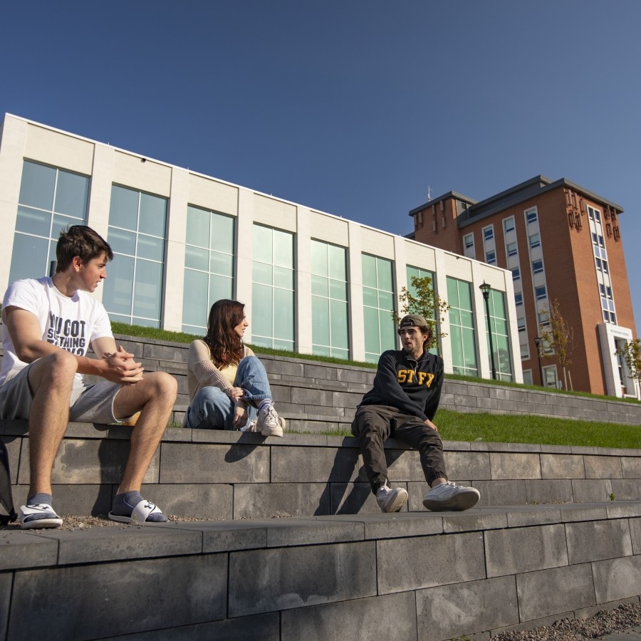 Students sitting on the brick located behind Mulroney Hall on a sunny day.