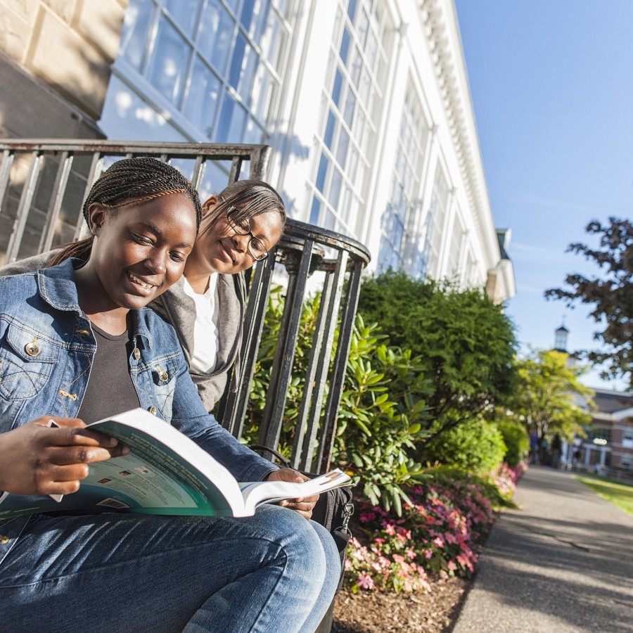 Two students reading a book while sitting outside on Morrison Hall steps during a sunny day.