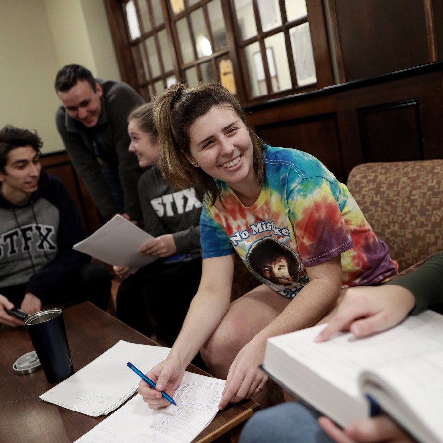 Students studying in the Bishops Hall lounge area. They are sitting on couches, using a table in the center for their notes.
