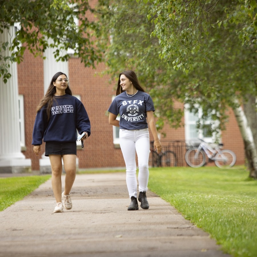 Students walking outside on a sunny day. There are trees around them and a bike rack in the background.