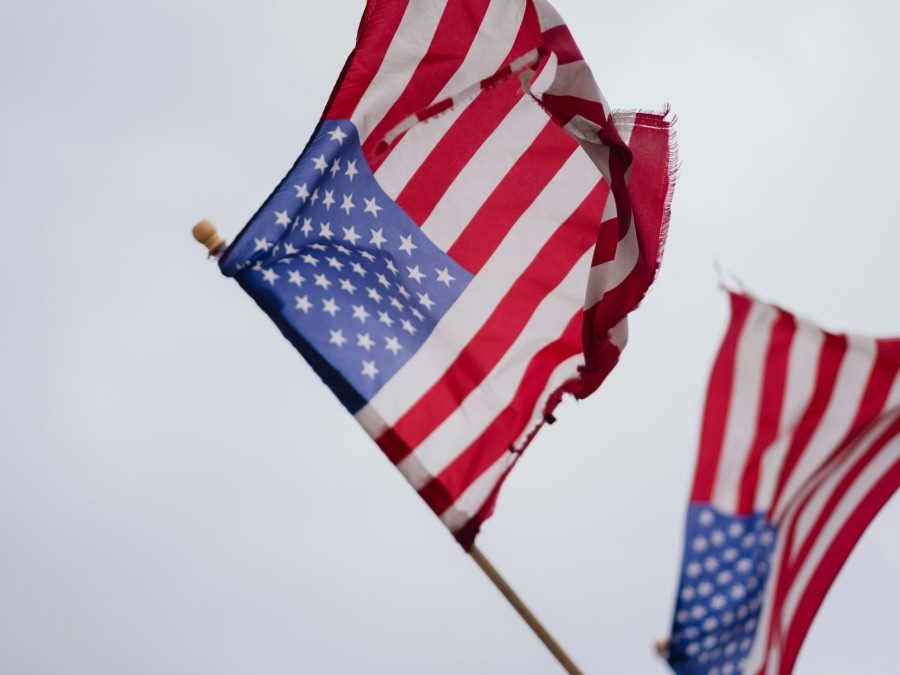 Two tattered US flags against a grey sky.