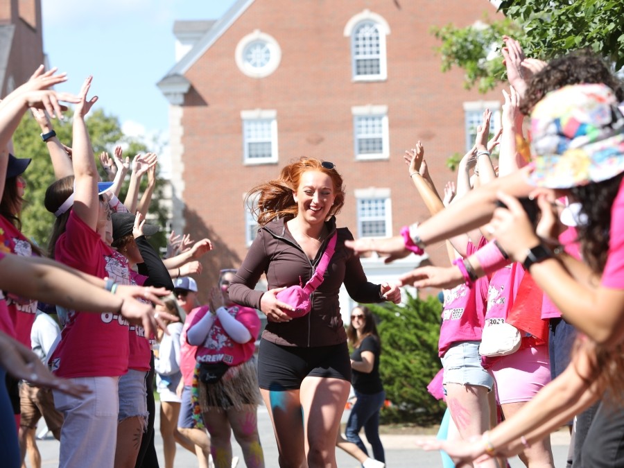 A happy student runs between two lines of cheering people in pink shirts