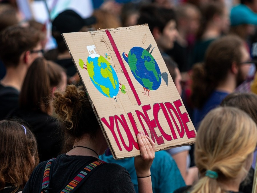Climate protestor holding a sign with two planet Earths depicted, one seemingly ruled by corporations, and the words "You Decide" underneath